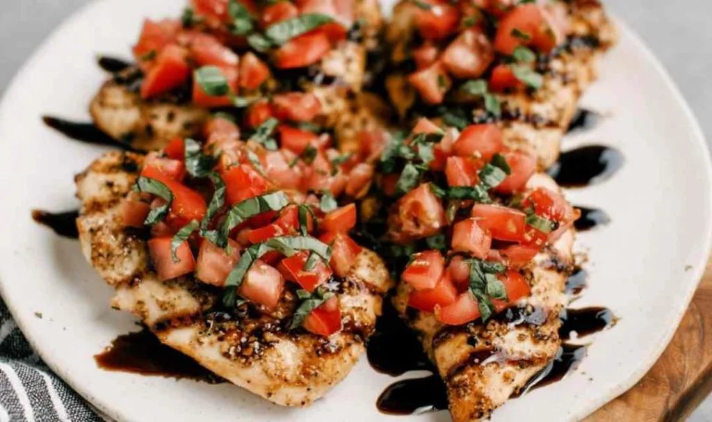 Bruschetta chicken breasts topped with fresh tomato and basil on a white serving platter