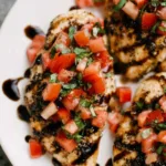 Bruschetta chicken breasts topped with fresh tomato and basil on a white serving platter