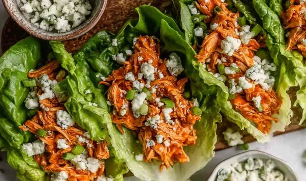 Buffalo Chicken Lettuce Wraps arranged on a platter with blue cheese crumbles and fresh celery.