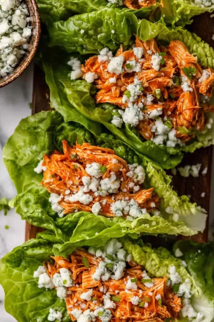 Buffalo Chicken Lettuce Wraps arranged on a platter with blue cheese crumbles and fresh celery.