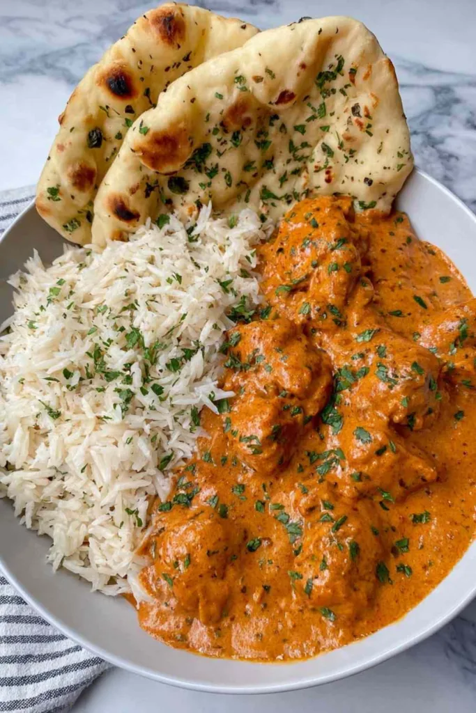 Creamy Butter Chicken Recipe served in a white bowl with basmati rice and naan bread.