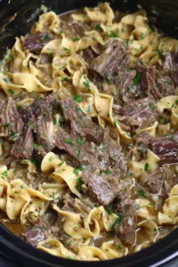 Crock pot beef and noodles in a bowl garnished with fresh parsley