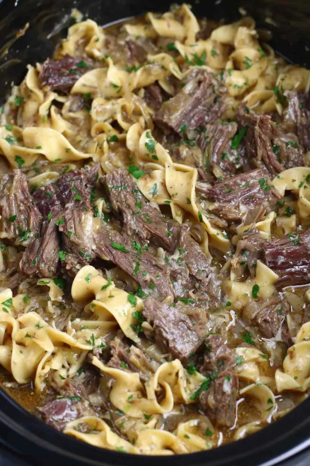 Crock pot beef and noodles in a bowl garnished with fresh parsley
