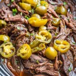 Crockpot Mississippi pot roast with shredded beef, whole pepperoncini peppers and butter in a slow cooker