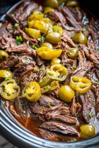 Crockpot Mississippi pot roast with shredded beef, whole pepperoncini peppers and butter in a slow cooker