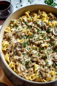 A creamy skillet of Ground Turkey Stroganoff with egg noodles and parsley in a cast iron pan.