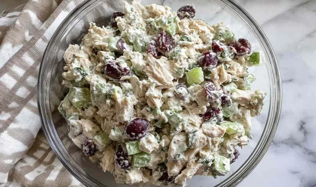 Healthy chicken salad with Greek yogurt dressing being mixed in a large bowl with fresh dill, celery, and red onion