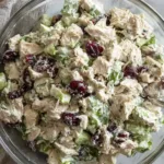 Healthy chicken salad with Greek yogurt dressing being mixed in a large bowl with fresh dill, celery, and red onion