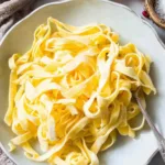 Smooth yellow batter for homemade keto egg noodles spread thinly on parchment paper inside a baking sheet ready for the oven.