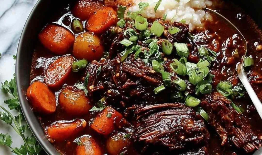 Korean Style Pot Roast shredded in a Dutch oven with gochujang braising sauce and green onion garnish