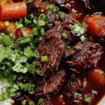 Korean Style Pot Roast shredded in a Dutch oven with gochujang braising sauce and green onion garnish