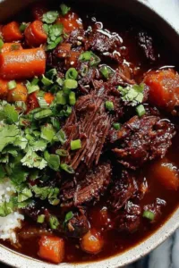 Korean Style Pot Roast shredded in a Dutch oven with gochujang braising sauce and green onion garnish