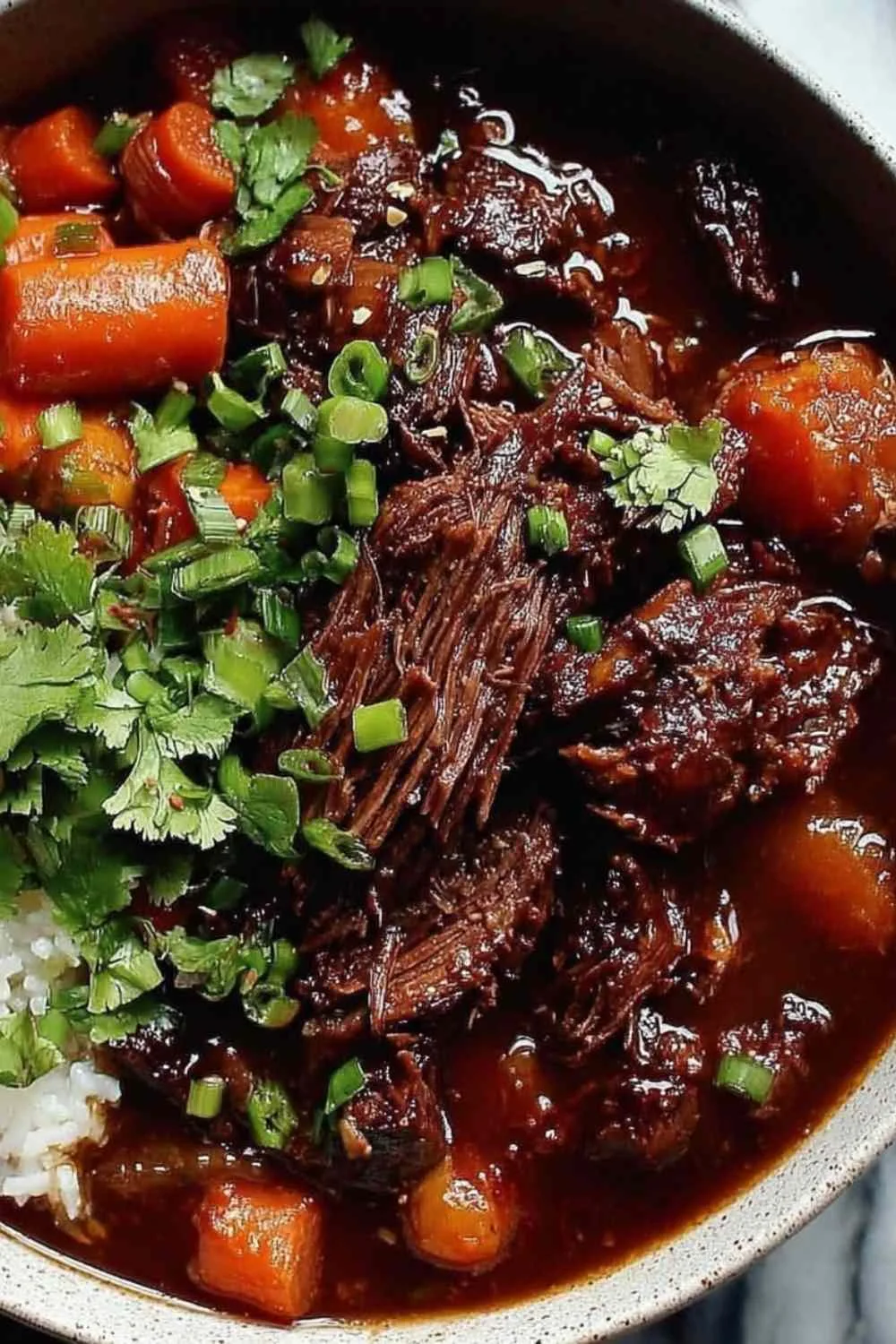 Korean Style Pot Roast shredded in a Dutch oven with gochujang braising sauce and green onion garnish