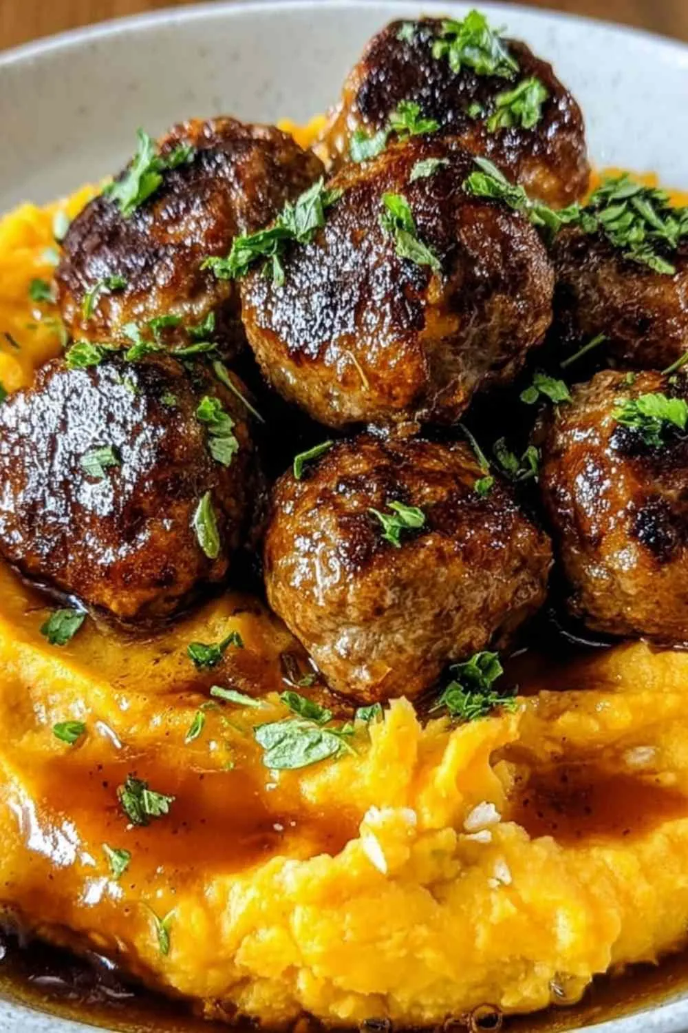 Pork meatballs with sweet potato mash drizzled with bourbon maple sauce on a white plate.
