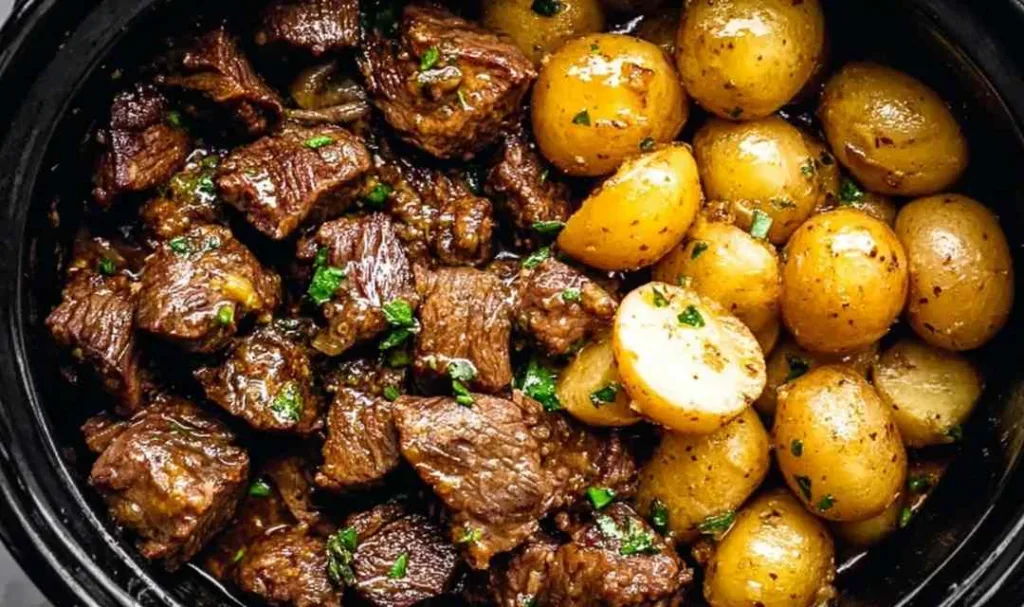 Slow cooker garlic butter beef bites with potatoes in a white bowl garnished with parsley