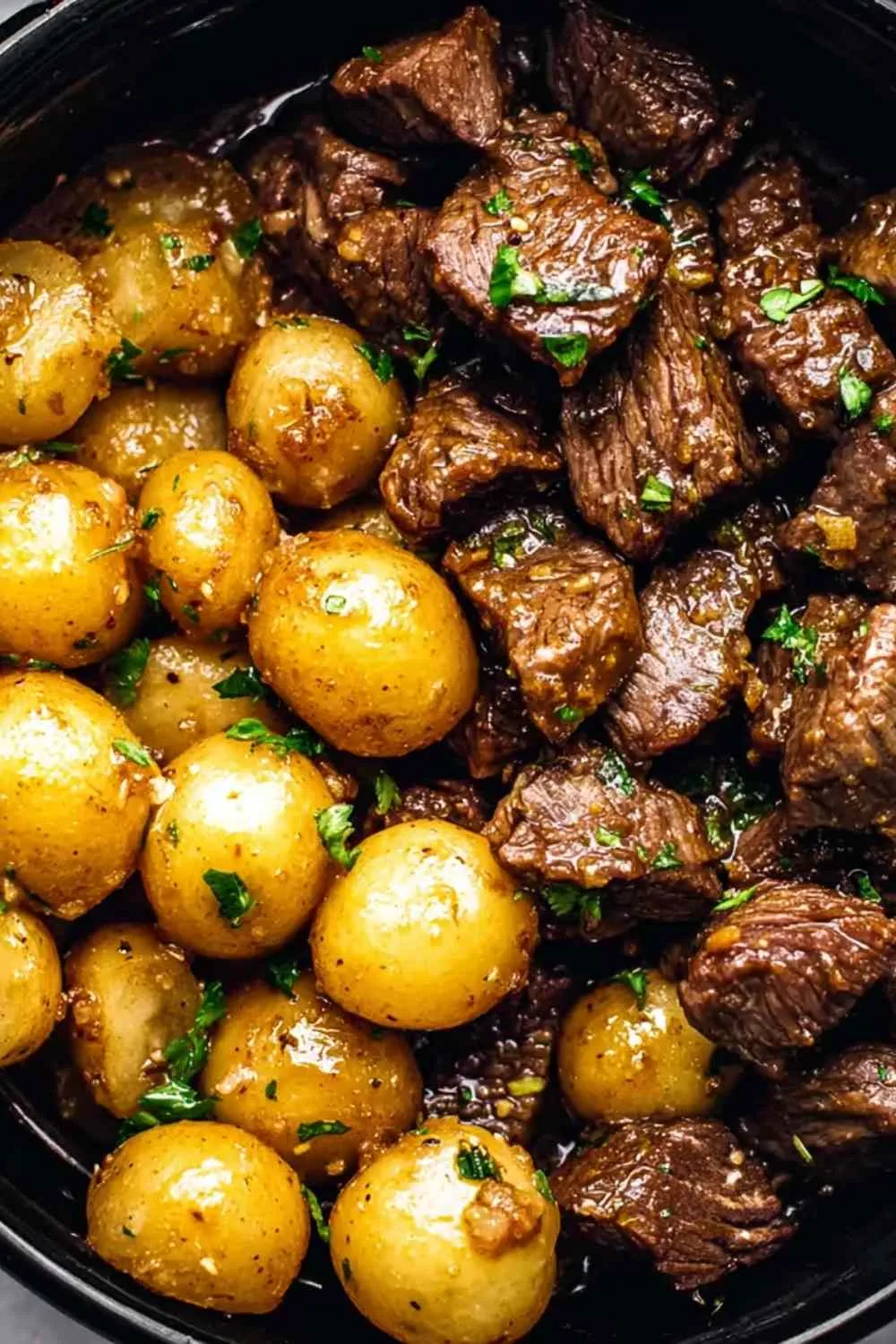 Slow cooker garlic butter beef bites with potatoes in a white bowl garnished with parsley
