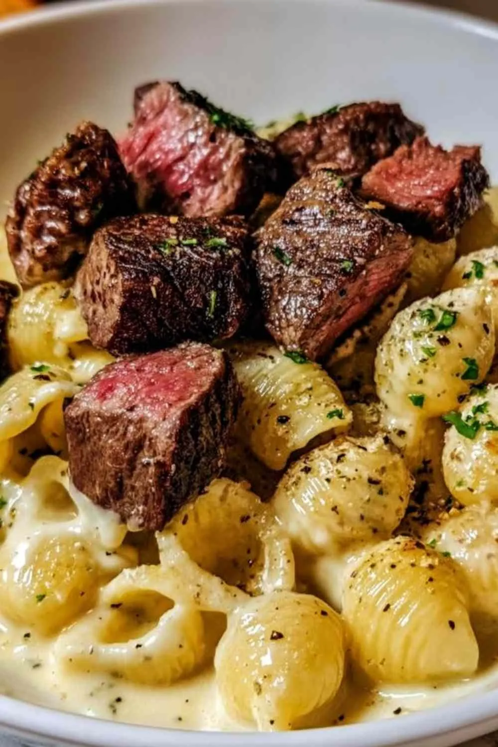 Steak bites and shell pasta in garlic butter Alfredo sauce served in a white bowl with parsley garnish