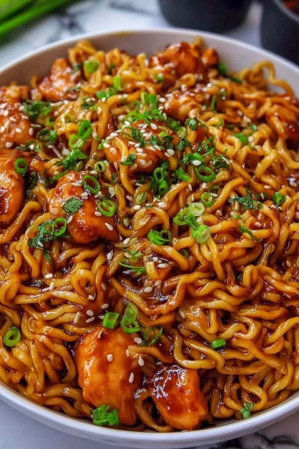 Sticky garlic chicken noodles in a skillet garnished with green onions and sesame seeds