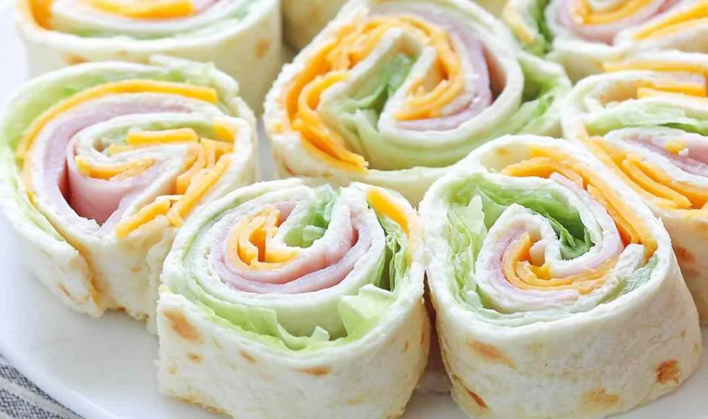 Hands rolling up a Turkey Cheddar Lunch Roll-Up filled with deli turkey, cheddar cheese, spinach, shredded carrots, and red bell pepper on a flour tortilla