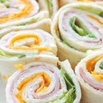Hands rolling up a Turkey Cheddar Lunch Roll-Up filled with deli turkey, cheddar cheese, spinach, shredded carrots, and red bell pepper on a flour tortilla