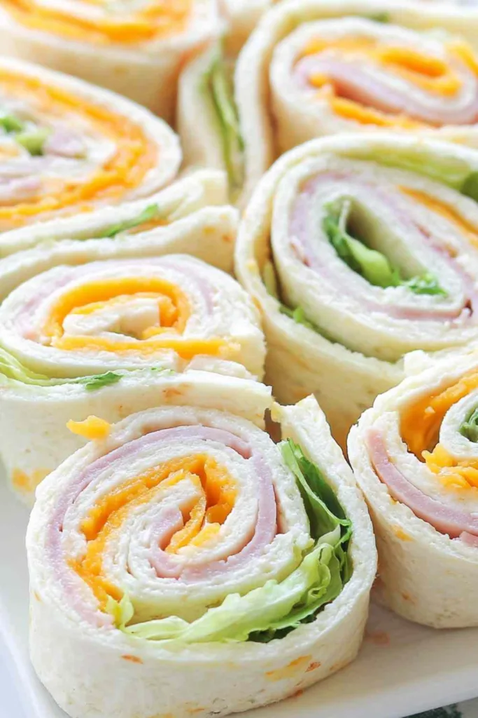 Hands rolling up a Turkey Cheddar Lunch Roll-Up filled with deli turkey, cheddar cheese, spinach, shredded carrots, and red bell pepper on a flour tortilla