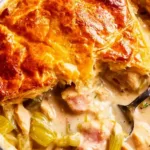Chicken and leek pie with golden puff pastry crust bubbling in a white baking dish