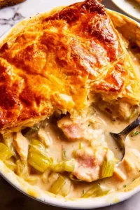 Chicken and leek pie with golden puff pastry crust bubbling in a white baking dish