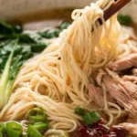 Chinese noodle soup broth simmering with garlic and ginger in a saucepan