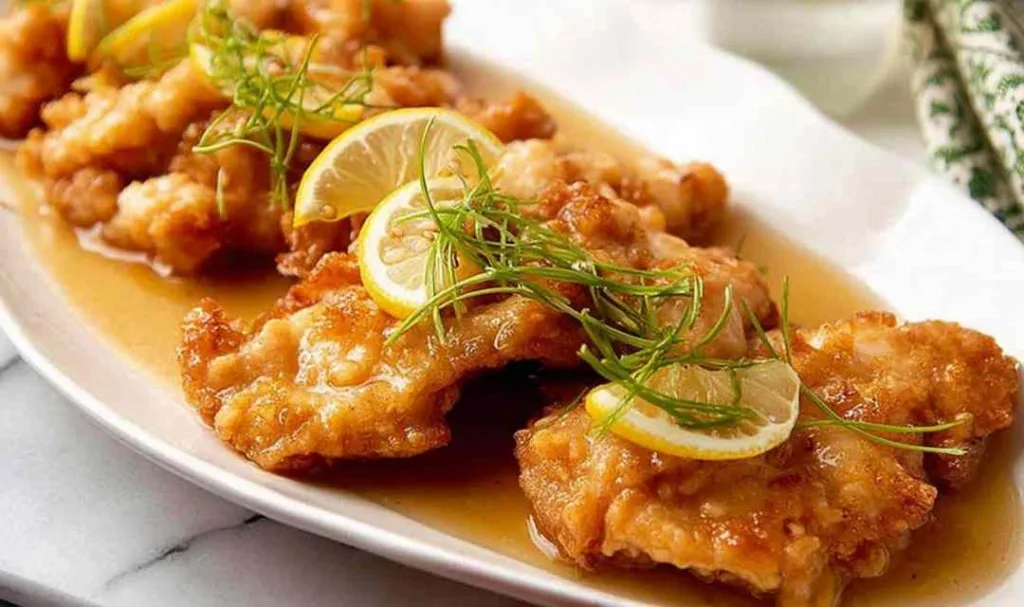 Crispy Chinese lemon chicken sliced on a white plate with lemon sauce and green onions