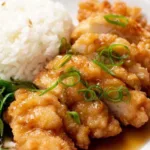 Crispy Chinese lemon chicken sliced on a white plate with lemon sauce and green onions