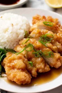 Crispy Chinese lemon chicken sliced on a white plate with lemon sauce and green onions