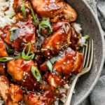 Crock pot bourbon chicken served over brown rice and topped with chopped green onions in a white bowl
