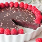 dark chocolate raspberry tart slice on white plate with fresh raspberries