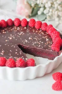 dark chocolate raspberry tart slice on white plate with fresh raspberries