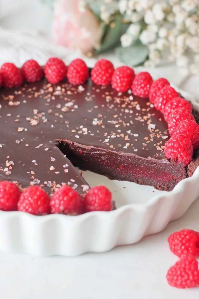 dark chocolate raspberry tart slice on white plate with fresh raspberries