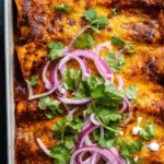 red chicken enchiladas baked in a 9x13 dish with melted cheese and cilantro