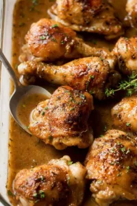 gravy baked chicken thighs and drumsticks in a baking pan with rich dark gravy