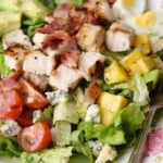 Grilled chicken Cobb salad with romaine, bacon, eggs, avocado, tomatoes, and blue cheese on a white plate