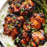 Grilled honey garlic chicken thighs on a serving plate garnished with sesame seeds and green onions