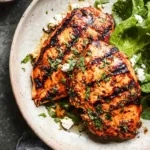 juicy grilled chicken breast on a white plate with fresh herbs and lemon