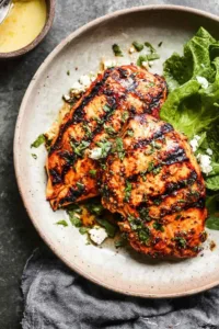 juicy grilled chicken breast on a white plate with fresh herbs and lemon