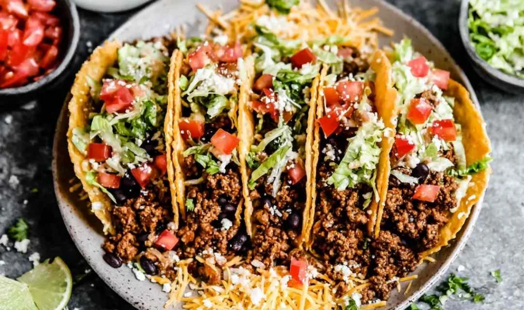 Crispy ground beef tacos in homemade fried corn tortilla shells topped with shredded lettuce, tomatoes, and cheddar cheese