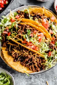 Crispy ground beef tacos in homemade fried corn tortilla shells topped with shredded lettuce, tomatoes, and cheddar cheese