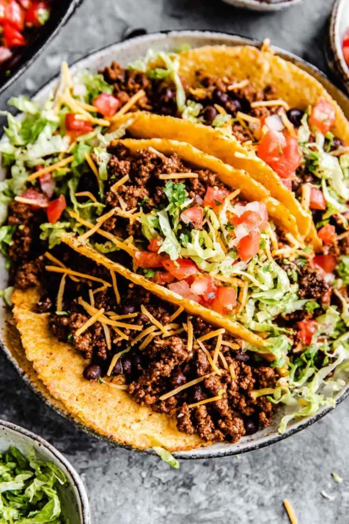 Crispy ground beef tacos in homemade fried corn tortilla shells topped with shredded lettuce, tomatoes, and cheddar cheese