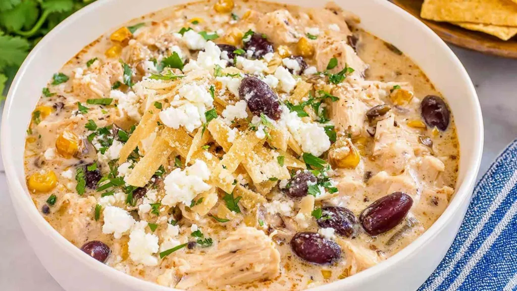 A white bowl of Mexican chicken and street corn chowder topped with cotija cheese, cilantro, Tajin, and a lime wedge