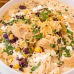 A white bowl of Mexican chicken and street corn chowder topped with cotija cheese, cilantro, Tajin, and a lime wedge