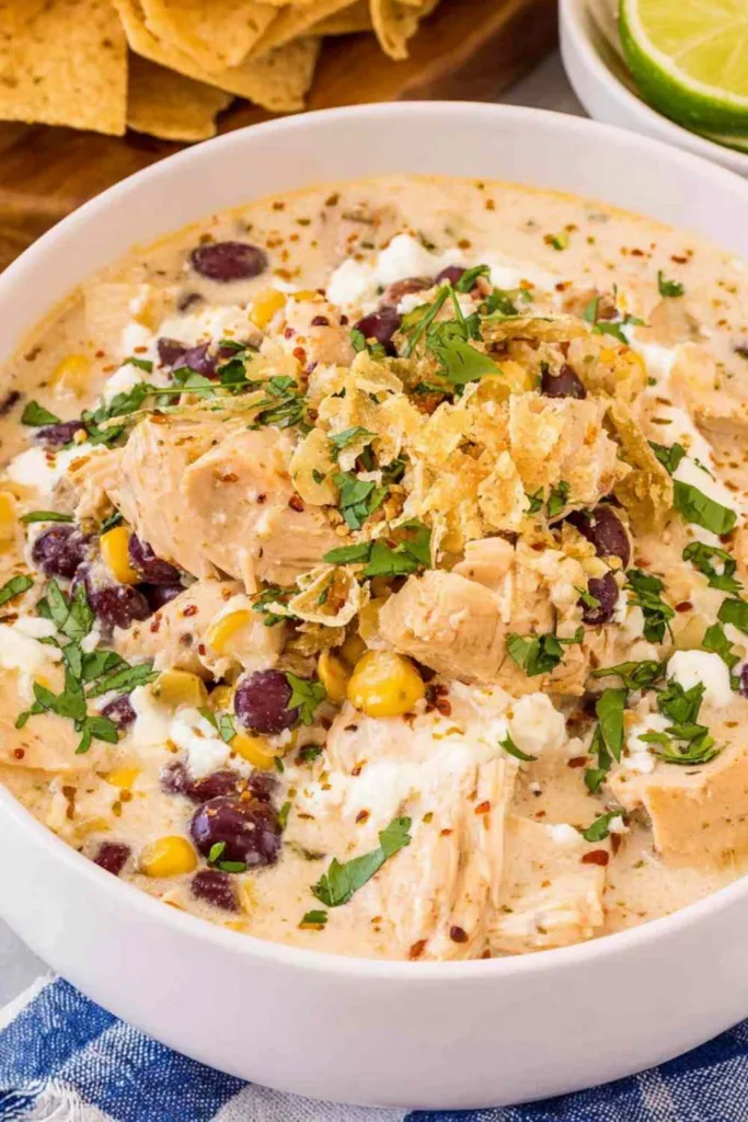 A white bowl of Mexican chicken and street corn chowder topped with cotija cheese, cilantro, Tajin, and a lime wedge