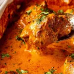 one pan baked butter chicken in a white baking dish with golden chicken thighs and rich orange sauce