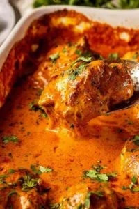one pan baked butter chicken in a white baking dish with golden chicken thighs and rich orange sauce