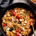 One pot Greek chicken orzo in a cast iron skillet with feta and cherry tomatoes
